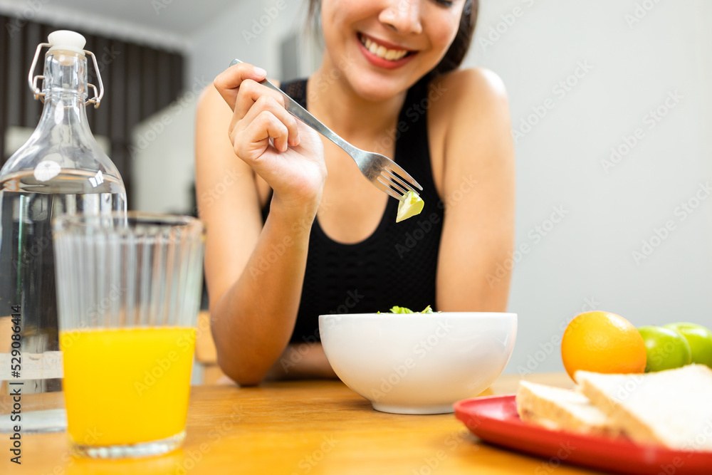 Young female sportswear eating organic greens vegetable salad in weight loss diet and wellness on table. Beautiful woman happily eat a healthy salad breakfast in kitchen in the morning. Young female sportswear eating organic greens vegetable salad in weight loss diet and wellness on table. Beautiful woman happily eat a healthy salad breakfast in kitchen in the morning.