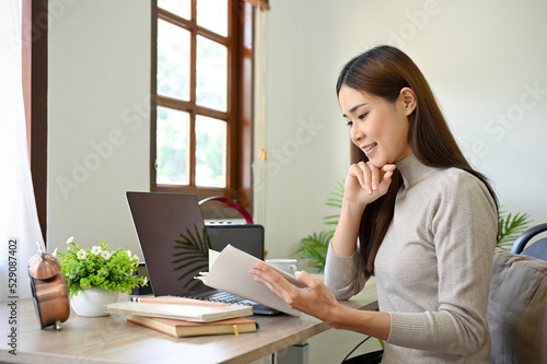 Attractive and relaxed young Asian woman reading a book at her office desk. © bongkarn