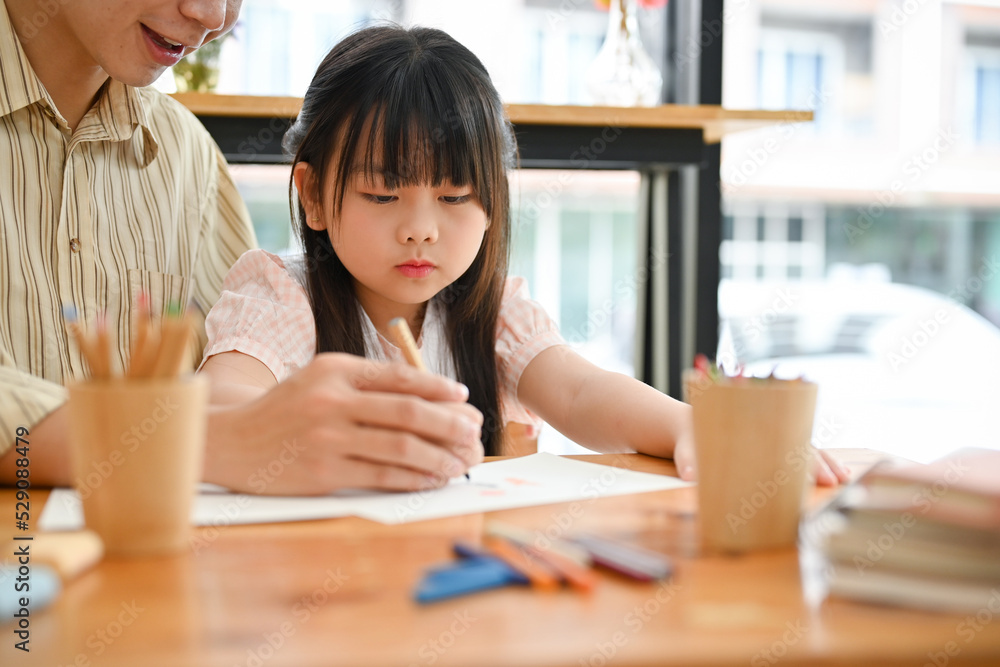 Pretty young Asian girl concentrating doing homework, having an art class with her private teacher. Pretty young Asian girl concentrating doing homework, having an art class with her private teacher.