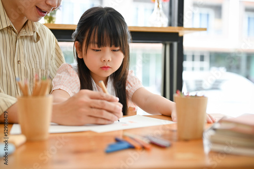 Pretty young Asian girl concentrating doing homework, having an art class with her private teacher.