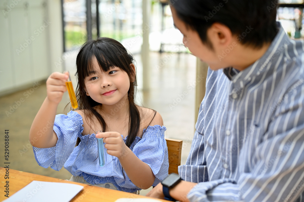 Bright young Asian girl holding a test tube, studying science with her school teacher. Bright young Asian girl holding a test tube, studying science with her school teacher.