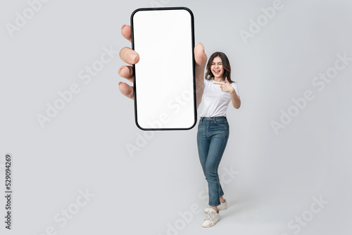 Full length of cheerful Asian woman smiling with showing cellphone blank screen with empty space for mobile app on screen. Isolated in studio pink background. Creative collage. photo