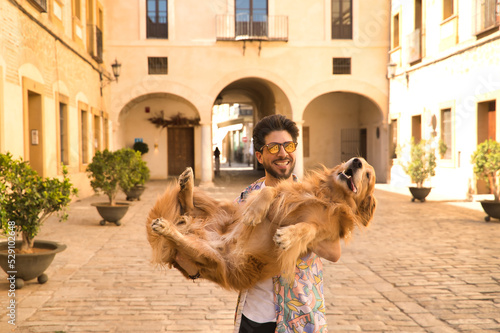 Young Hispanic man with beard and sunglasses holding his dog in his arms very happy. Concept animals, dogs, love, pets, golden.