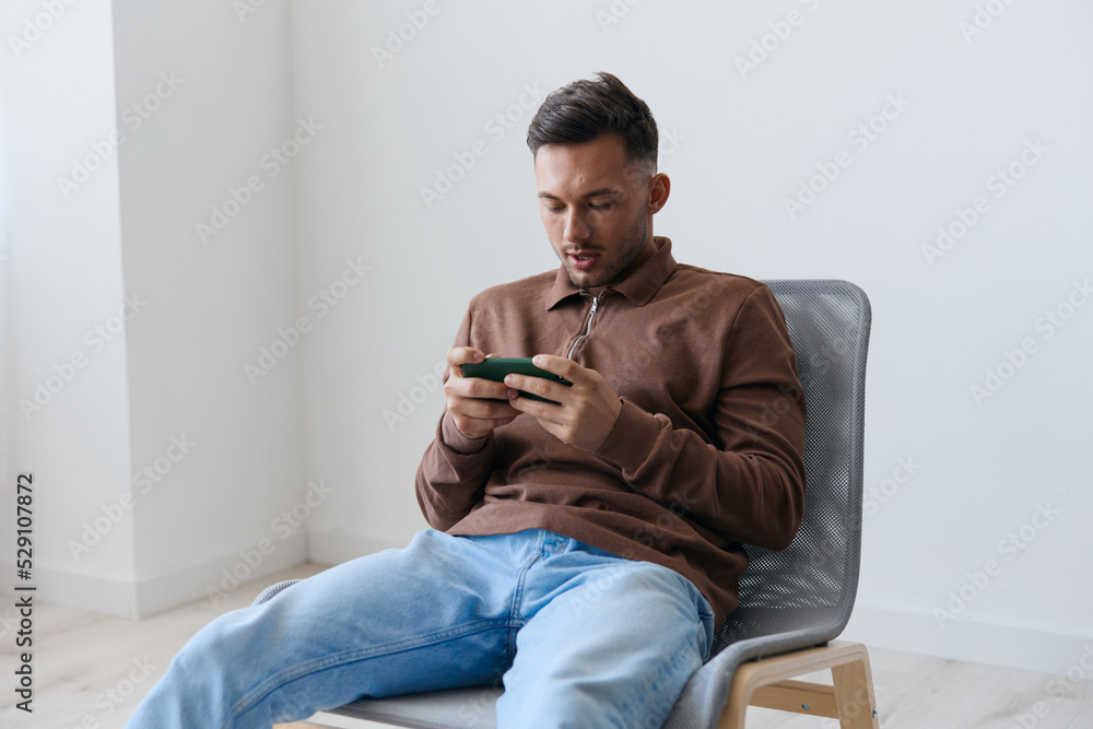 Enjoyed focused confused attractive try to win enthusiastically playing in exciting raising game looks at screen. Happy guy relaxing with phone chatting with friends. Mobile App concept. Copy space Enjoyed focused confused attractive try to win enthusiastically playing in exciting raising game looks at screen. Happy guy relaxing with phone chatting with friends. Mobile App concept. Copy space