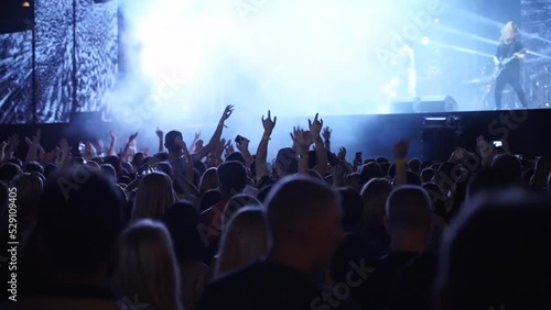 People silhouettes jump waving and clapping hands, crazy dancing with hand-horns at live music concert at open air festival. Fans at favourite rock band performance.