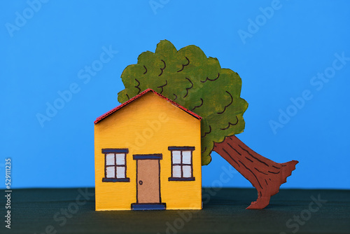 Yellow red toy cardboard house middle of frame dark green base blue background tree in roof