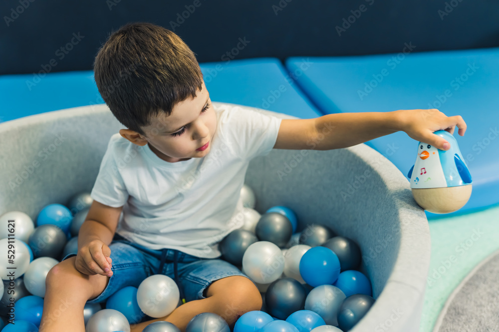 Toddler boy playing with a toy while sitting in a ball pit full of