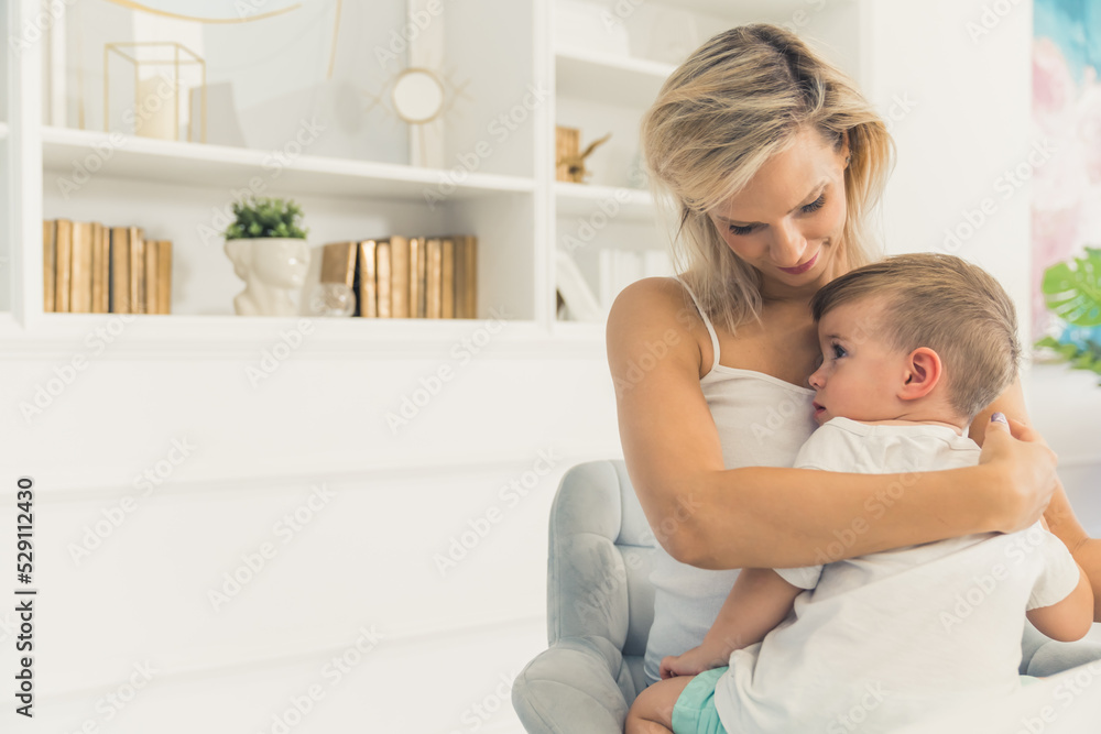 Mother and son. Modern living room interior. Beautiful young adult caucasian woman hugging her cute sleepy son. Time for a nap. High quality photo