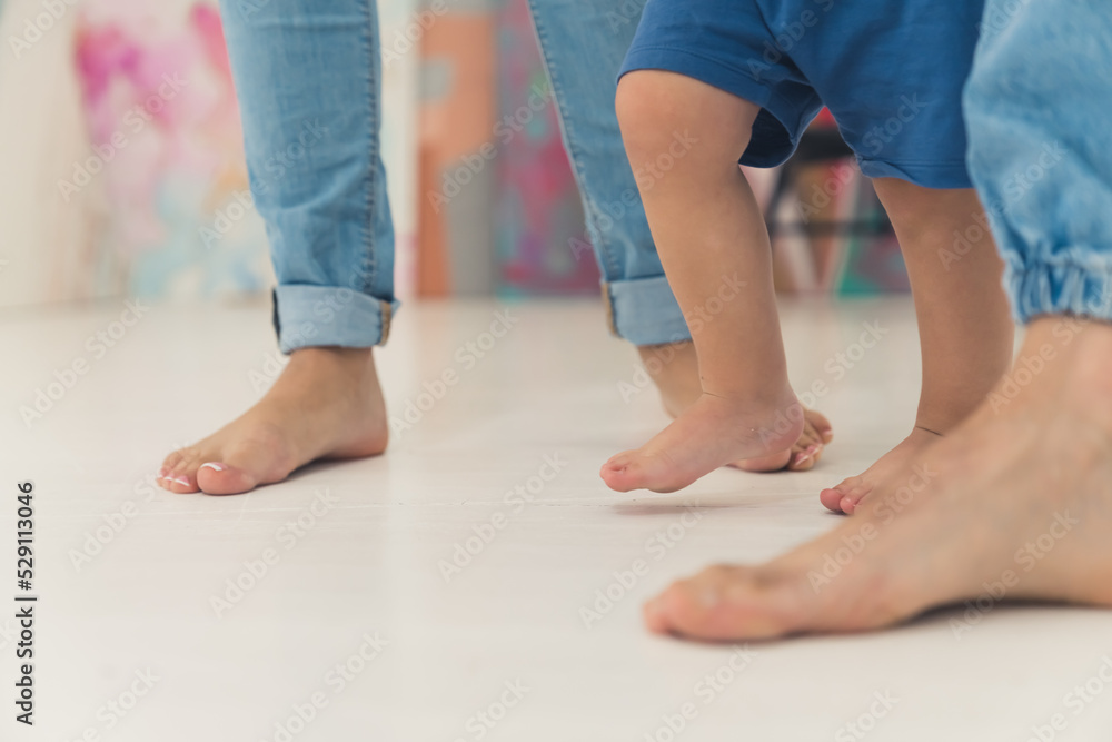 Closeup indoor shot of three pairs of bare feet of caucasian people walking on white floor. Two adult parents in jeans and their little kid. Parenthood concept. High quality photo