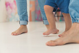 Closeup indoor shot of three pairs of bare feet of caucasian people walking on white floor. Two adult parents in jeans and their little kid. Parenthood concept. High quality photo