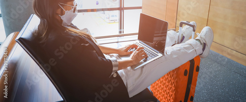 Selective focus of woman hand unrecognizable wearing marsk with digital nomad sitting alone and typing on her laptop during the day at Airport photo