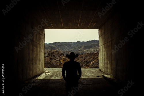 Silhouette of adult man in cowboy hat standing in entrance of a tunnel