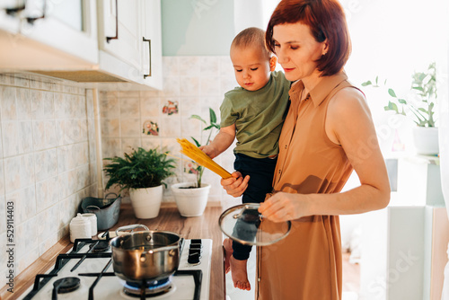 Happy mom with her child cooking at the kitchen. Cozy home and routine duties