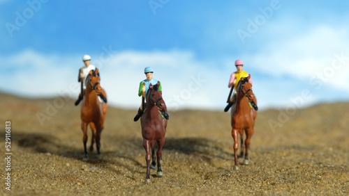 Miniature people toy figure photography. A jockey man riding horse at farm, sand desert land field.
