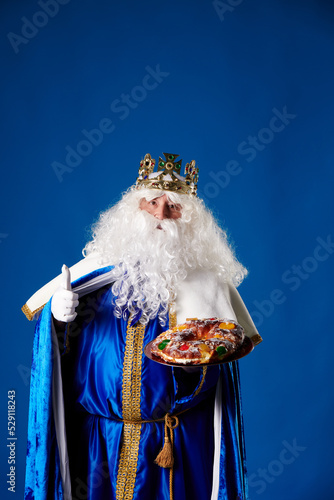smiling wise man holding a "roscón de reyes" in his hand on a blue background