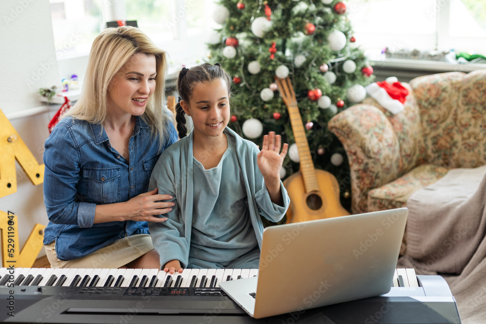 Mom teaching her daughter to play a new year song on the piano on christmas eve in a decorated room, new year mood Mom teaching her daughter to play a new year song on the piano on christmas eve in a decorated room, new year mood
