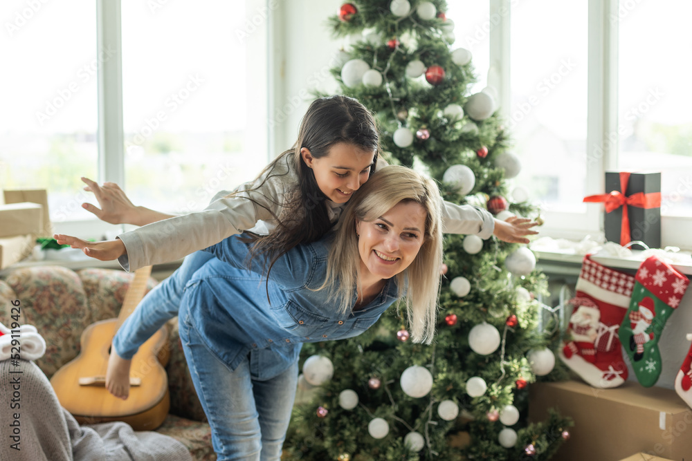 Merry Christmas and Happy Holidays. Cheerful mother and her cute daughter girl exchanging gifts. Mom and little child having fun near tree indoors. Loving family with presents in room Merry Christmas and Happy Holidays. Cheerful mother and her cute daughter girl exchanging gifts. Mom and little child having fun near tree indoors. Loving family with presents in room