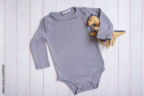 Grey baby bodysuit top view. Mock up for logo, text or design on wooden background. Flat lay with dinosaur