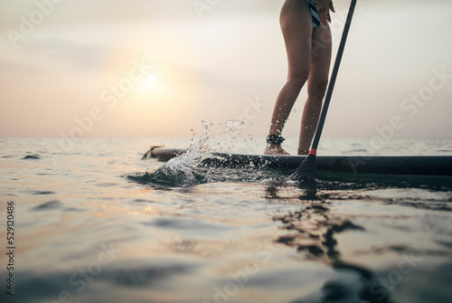 Close up of woman paddleboarding on sunset sea