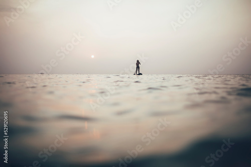 Woman silhouette paddleboarding on sunset sea