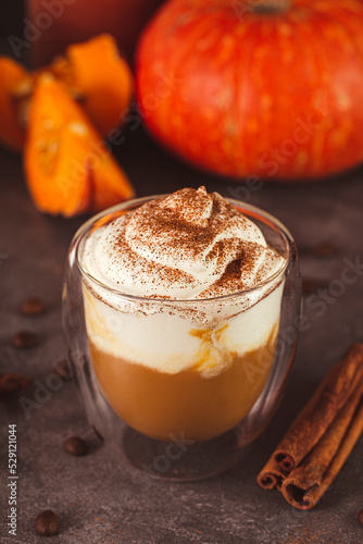 A glass of autumn pumpkin latte with whipped cream and spices. Coffee with pumpkin and cinnamon on a dark background vertical photo