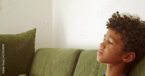 a frustrated boy is at home, sitting on the couch and looking away with a frown, close to crying, acting up.