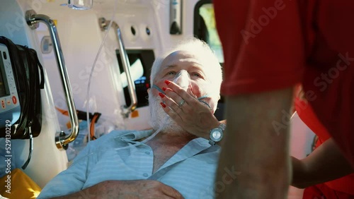 Senior male patient receiving advanced emergency medical care in ambulance. Paramedic holding patient head wearing oxygen mask in ambulance photo