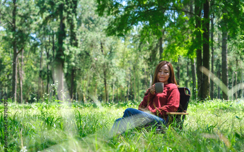 Portrait image of a beautiful young asian woman drinking coffee while sitting on a chair in the park © Farknot Architect
