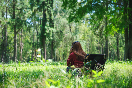Rear view of a young woman enjoy listening to music with headphone while sitting on a camping chair in the park