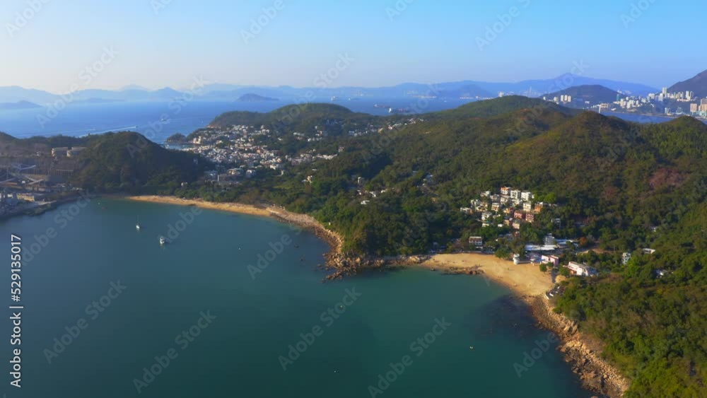 drone shot traveling to the left next to a urbanized tropical island with some villages and beach among the mountains and forest during a sunny day. drone shot traveling to the left next to a urbanized tropical island with some villages and beach among the mountains and forest during a sunny day.