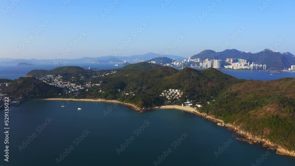 drone shot traveling forward above a tropical island with some villages and beach among the mountains and forest during a sunny day. Another island with skyscrapers is in the distance. drone shot traveling forward above a tropical island with some villages and beach among the mountains and forest during a sunny day. Another island with skyscrapers is in the distance.