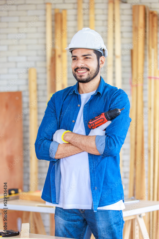 Asian Indian professional male engineer architect foreman labor worker wears safety hard helmet and gloves standing smiling holding thumb up and electric power drill machine in home construction site Asian Indian professional male engineer architect foreman labor worker wears safety hard helmet and gloves standing smiling holding thumb up and electric power drill machine in home construction site