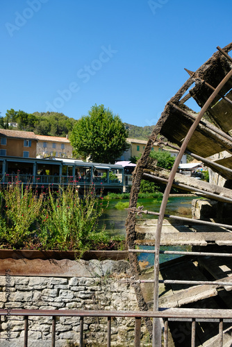 The old wooden water wheel on the Sorgue river and restaurant background. Fontaine de Vaucluse, France. Famous place.