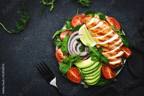 Fresh vegetable salad with grilled chicken fillet, spinach, tomatoes, avocado and red onion with olive oil on black background.. Healthy, detox, ketogenic diet food.. Top view