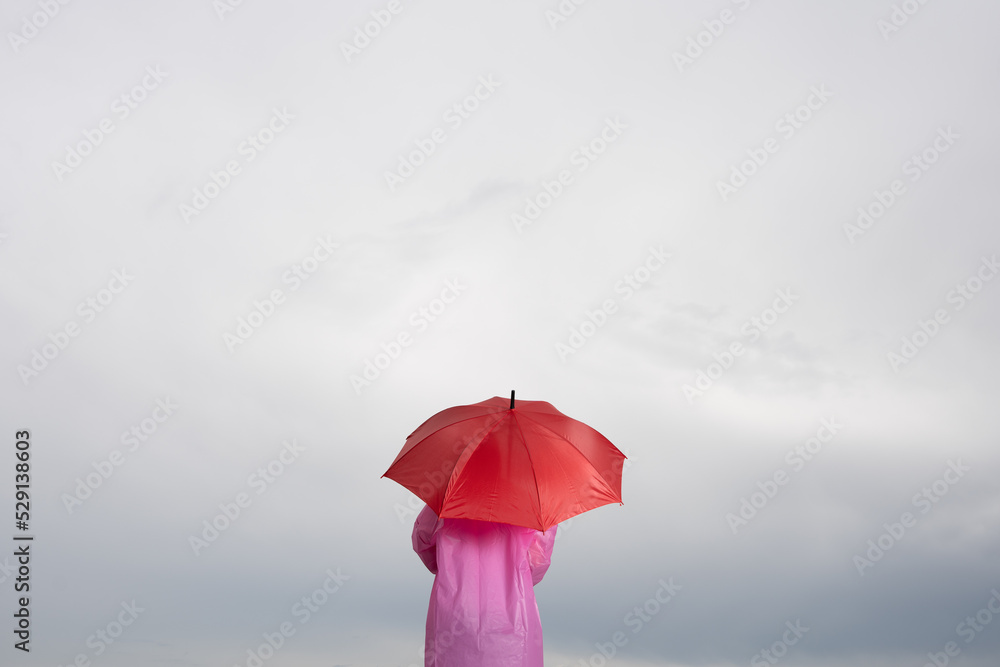 Rear view of person holding red umbrella under cloudy sky. Bad weather concept