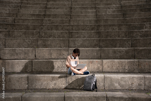 Teenager boy working on laptop sitting on staircase with dramatic lighting