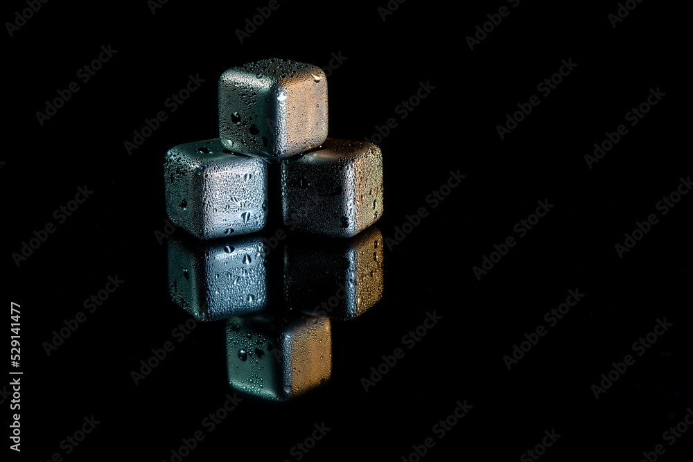 Stainless steel cubes simulating ice for cooling drinks on a black surface with a reflection.