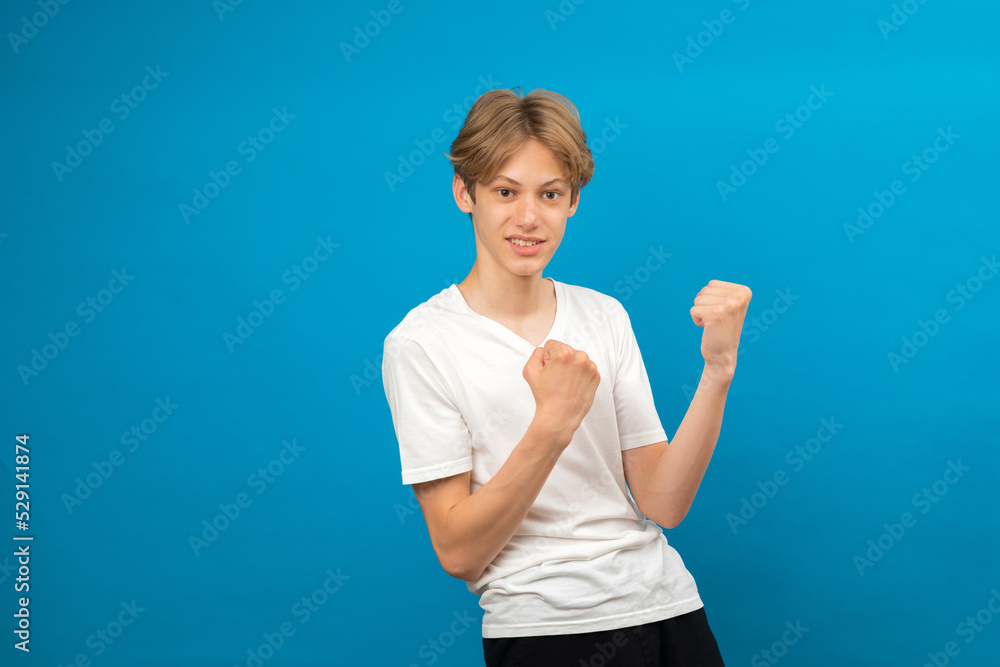 Extremely excited teen boy shouting making yes gesture, amazed with his victory, triumph. Indoor studio shot isolated on blue background Extremely excited teen boy shouting making yes gesture, amazed with his victory, triumph. Indoor studio shot isolated on blue background