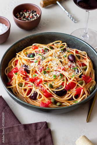 Spaghetti pasta Alla Puttanesca with capers, Kalamata olives, cheese, tomatoes and anchovies. Italian food.