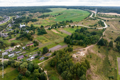 aerial panoramic view of green village with houses, barns and gravel road in forest