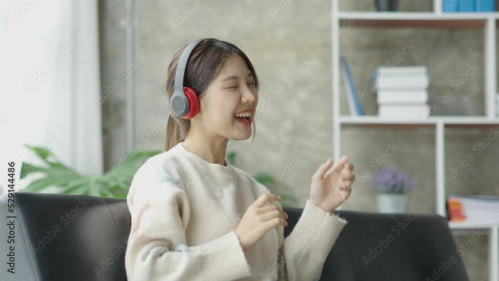 Beautiful and cute young Asian woman wearing headphone sitting on sofa and using smartphone listening to music happily and relaxing listening to music at her home. Beautiful and cute young Asian woman wearing headphone sitting on sofa and using smartphone listening to music happily and relaxing listening to music at her home.