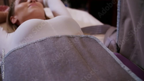 Young woman doing anti-cellulite pressotherapy procedure in beauty spa salon. Beauty therapist fixing costume belts and conducting pressotherapy procedure. Cellulite reducing treatment