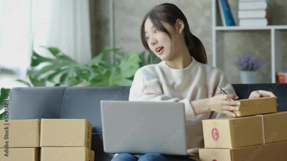 Smiling Asian online business owner prepares parcels and check online orders for delivery to customers on his laptop computer. Online selling concept. Smiling Asian online business owner prepares parcels and check online orders for delivery to customers on his laptop computer. Online selling concept.