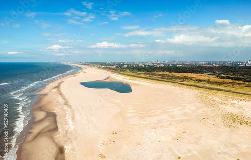 Aerial photo of the Zand Motor peninsula of the Kijkduin Beach of The Hague. In the background a large rain shower cloud and the city of The Hague skyline