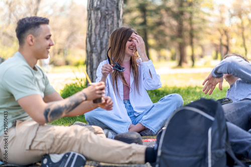 Group of cheerful friends spending time together while sitting on green lawn