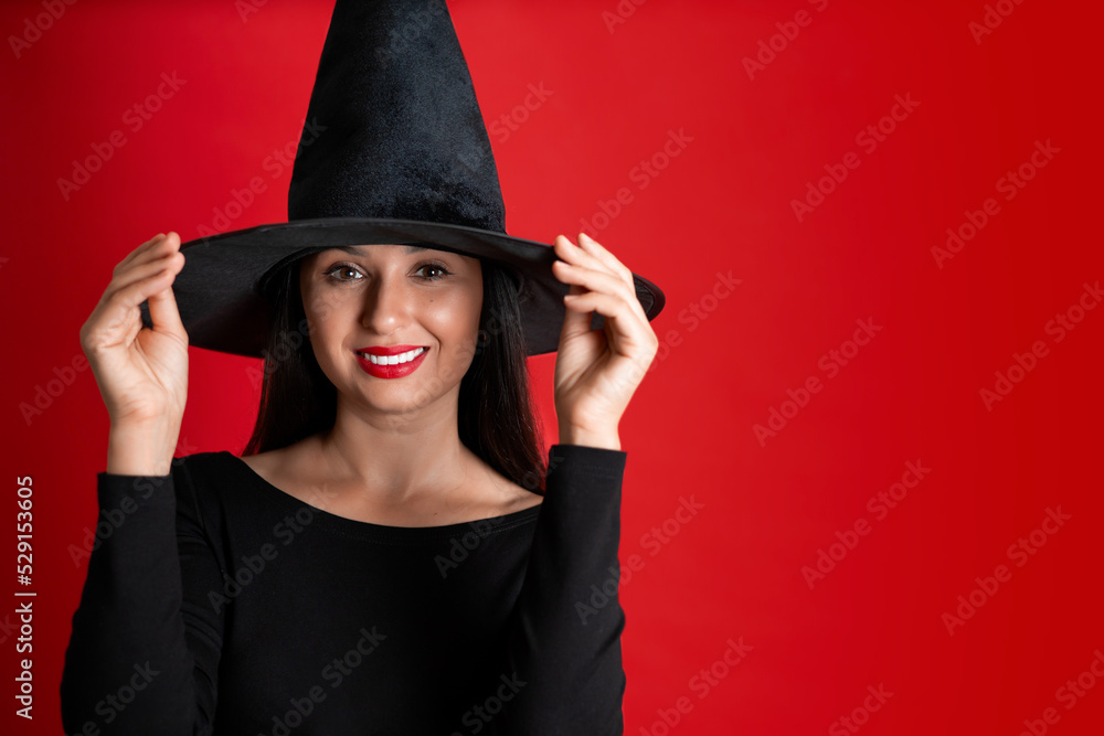 Halloween. A young beautiful woman in a witch's hat and a black dress on a red colored background. Space for text. Halloween. A young beautiful woman in a witch's hat and a black dress on a red colored background. Space for text.