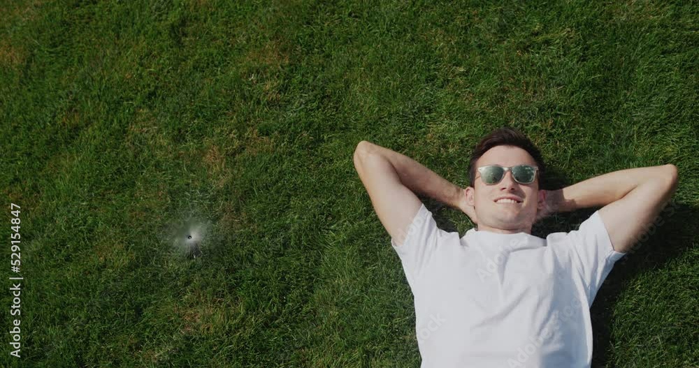 A young man lies under jets of water from automatic irrigation, escapes from the heat A young man lies under jets of water from automatic irrigation, escapes from the heat