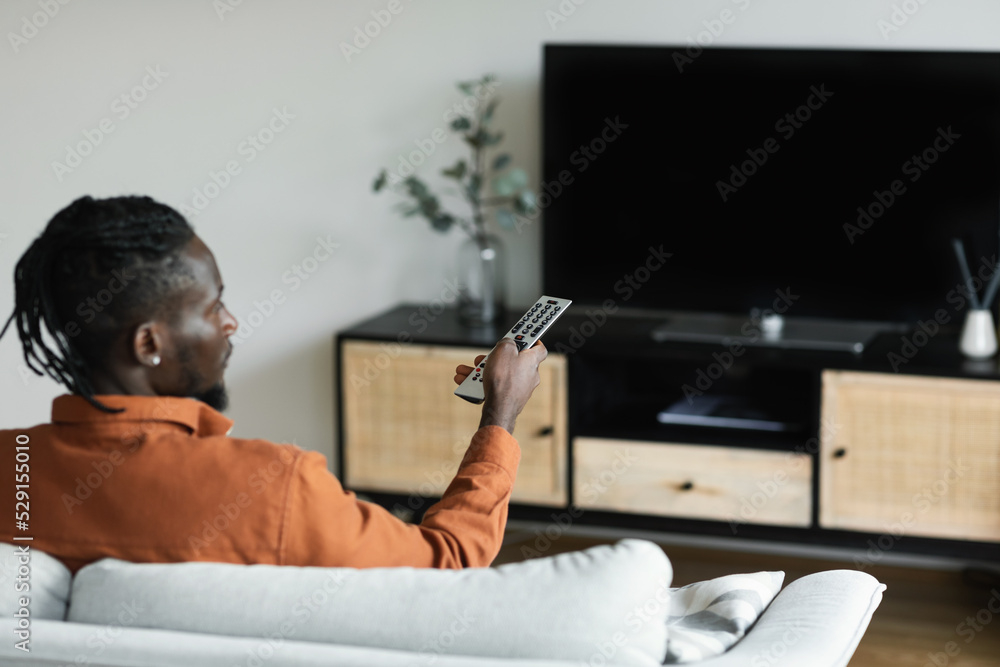 African american man watching television, pointing remote control at