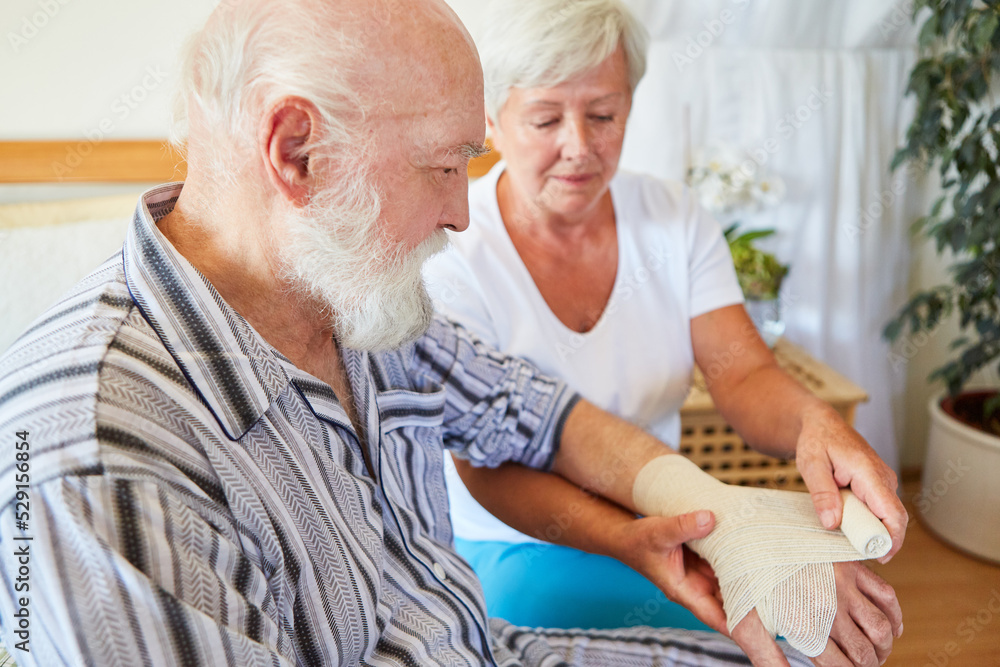 Pflegekraft beim Verband anlegen am Handgelenk von Senior Pflegekraft beim Verband anlegen am Handgelenk von Senior