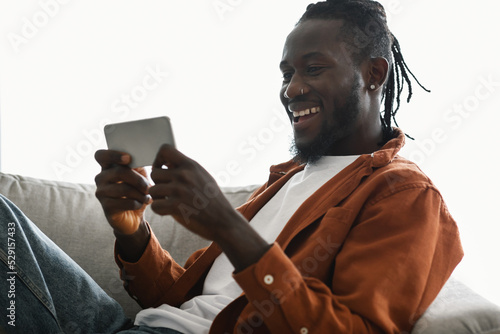 Foto Excited african american male gamer playing games on smartphone while chilling o